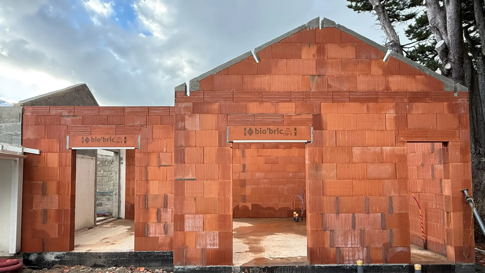 Élévation des murs en briques sur un chantier de construction, structure à moitié montée sous un ciel nuageux